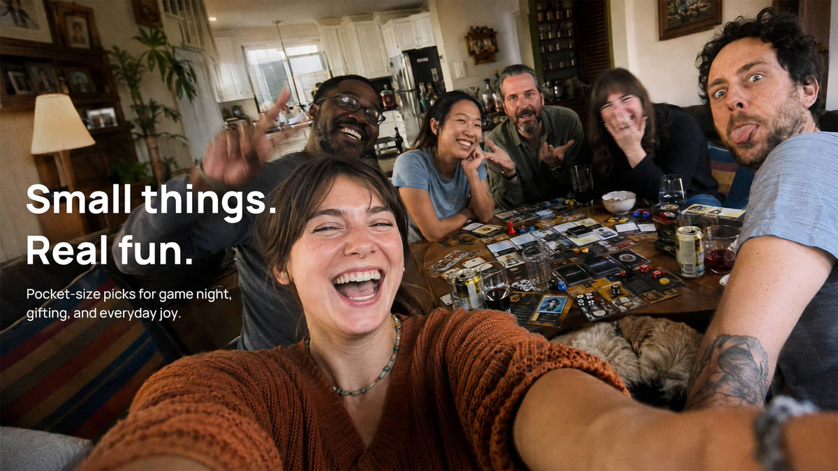 A group of five friends laughing and posing together around a wooden dining table in a cozy living room, with tabletop game accessories spread out. 