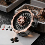 Rose gold and black metal D20 decision spinner displayed with playing cards and a bronze die.