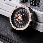 Rose gold and black metal D20 decision spinner beside playing cards and black dice.