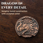 Copper 6-in-1 dice spinner with raised dragon relief displayed on a wooden tabletop.