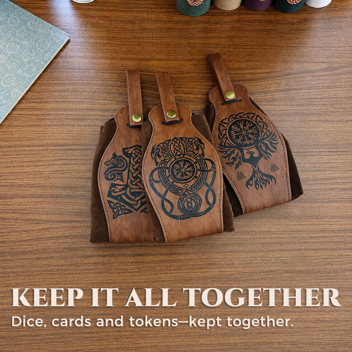 Three brown Norse belt pouches with different engraved mythic designs on a wooden table.