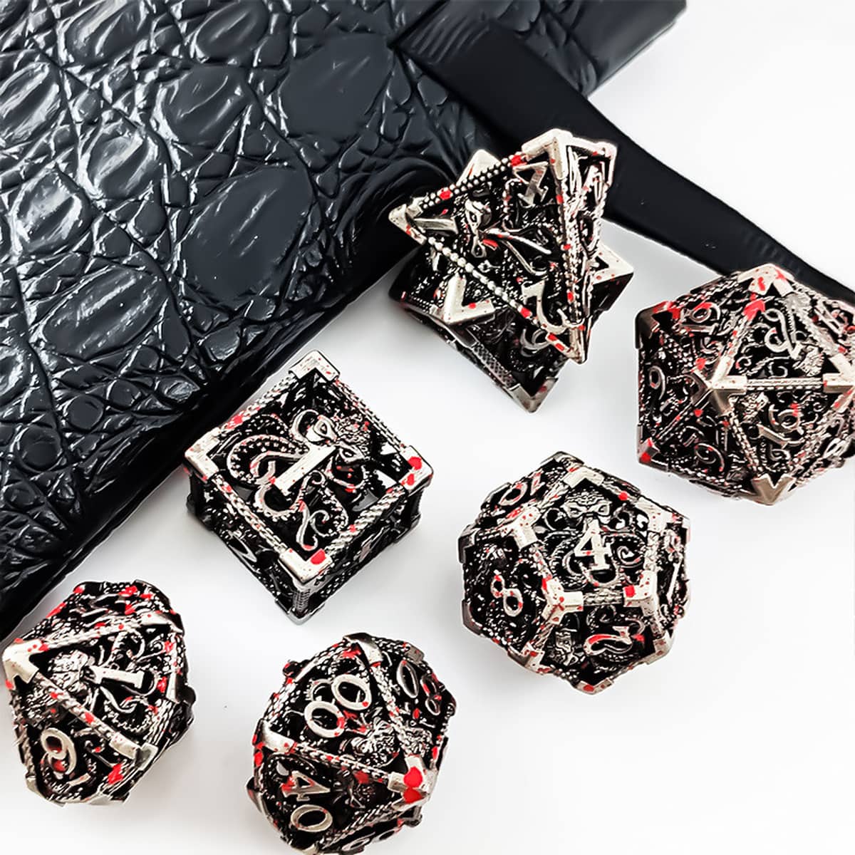 Silver hollow metal RPG dice set with red accents arranged beside a black dice bag.
